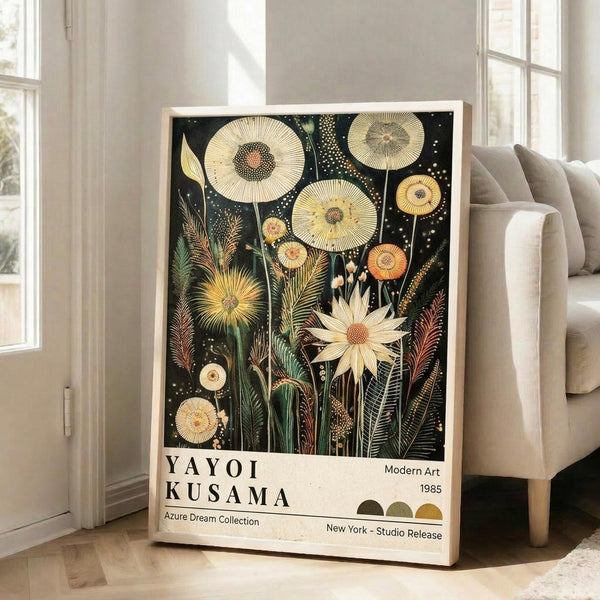 May include: Framed botanical art print leaning against white wall next to beige sofa in bright living room. Black background features golden yellow flowers, circular seed heads, feathery grasses, and white dotted patterns. White bottom section displays artist name and exhibition details. Natural wood frame, approximately 2-3 feet tall.