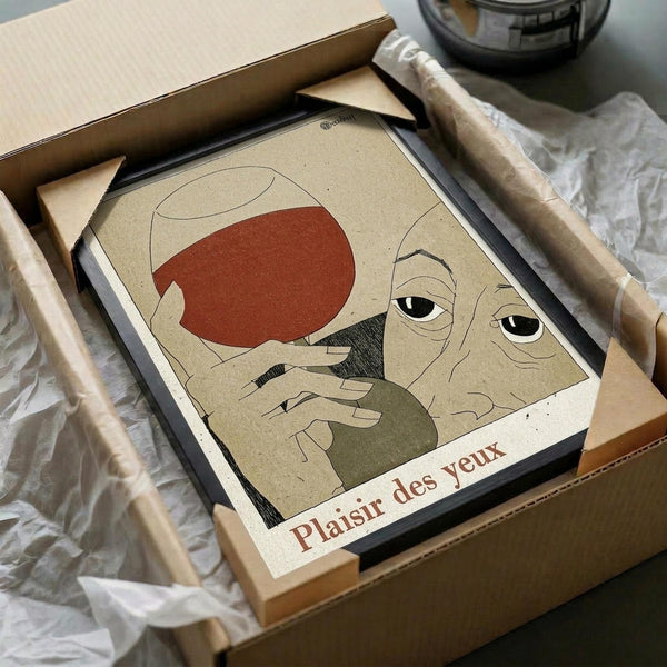 May include: Framed poster showing minimalist line art portrait of elderly man with mustache and beret in earth tones of red, beige, and black, with French text "Plaisir des yeux" at bottom. Artwork displayed in black frame inside cardboard shipping box with protective paper wrapping and wooden packing materials.