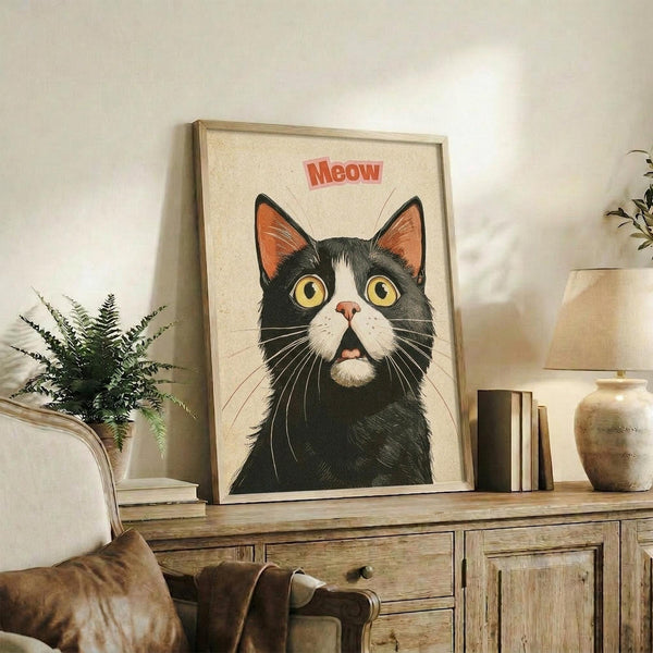 May include: Framed vintage-style poster featuring a black and white tuxedo cat with bright yellow eyes and orange ear interiors, with red "Meow" text above, displayed on rustic wooden sideboard alongside books, ceramic vase, and fern plant in cozy living room setting with beige armchair and neutral walls