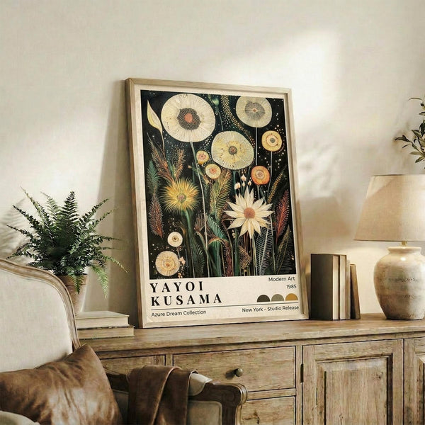 May include: Framed botanical art print with black background featuring stylized flowers and circular dandelion-like forms in cream, yellow, and coral tones. Print displays on rustic wooden console alongside fern plant, ceramic vase, and books in neutral-toned living room setting with beige armchair.