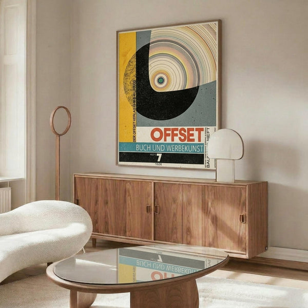 May include: Framed vintage Bauhaus poster with geometric design featuring circular concentric rings in yellow, gray, and black with "OFFSET" text, displayed above mid-century walnut credenza. Modern interior setting with white upholstered chair, brass floor lamp, oval glass coffee table, and neutral walls with natural lighting.