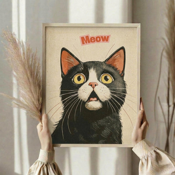 May include: Hands holding a framed poster featuring a black and white tuxedo cat with bright yellow eyes and orange inner ears, with "Meow" text in red lettering above. The artwork has a vintage illustration style on cream background in a light wood frame. Person wears cream ruffled sleeves and holds dried pampas grass, standing against white curtains.