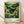 May include: A framed art print leaning against a white wall on light wood flooring. The poster features a lush green landscape with rolling hills, yellow flowering trees, and a golden sun with radiating lines in a Japanese woodblock print style. The artwork has rich emerald and forest green tones with bright yellow accents. Below the illustration is cream-colored text reading "YAYOI KUSAMA" with Japanese characters and "Modern Art 1950 TOKYO" along with small green circles. The print is