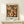 May include: Framed Paul Klee modern art poster displayed on light wood console table against white wall. Abstract artwork features coral pink figures with black stick-like bodies arranged in geometric grid pattern on dark textured background. Small wrapped gift box with greenery sits beside the wooden-framed print. Minimalist home decor styling with natural lighting creating soft shadows.