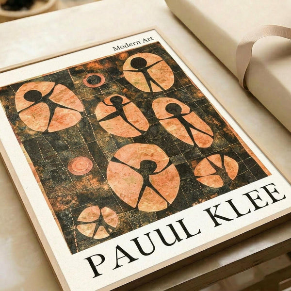 Modern art print featuring abstract human figures in coral and peach tones against a dark textured background with grid pattern. The artwork shows simplified stick-figure forms arranged in circular compositions. Print is matted in cream colored frame, lying flat on white surface next to rolled paper tubes. Artist name "PAUL KLEE" printed at bottom of piece.