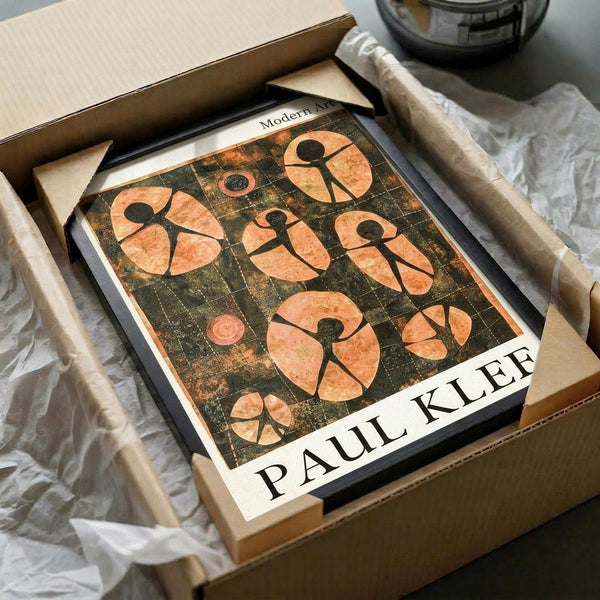 May include: Paul Klee art print in black frame, placed in cardboard shipping box with white tissue paper. The artwork features orange and rust-colored abstract human figures arranged in a grid pattern against a dark weathered background. Wooden dowels and glass bowl visible nearby on neutral surface.