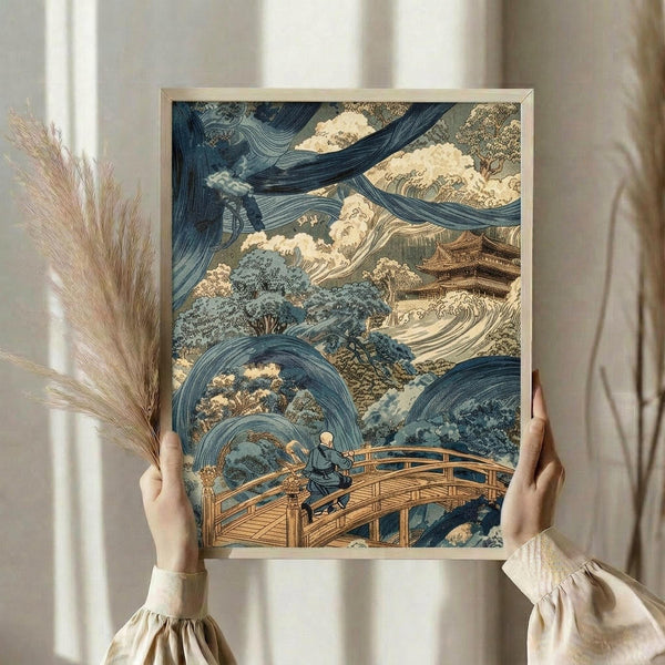May include: Person holding framed Japanese woodblock print showing monk crossing wooden bridge amid dramatic swirling blue waves and wind, with traditional pagoda in background. Print features classic ukiyo-e style with rich blues, golds, and earth tones. Hands visible wearing cream colored puffy sleeves, dried pampas grass decoration nearby against neutral curtained background.