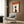 May include: Modern beige armchair with geometric pillow positioned below framed zen poster on wood-paneled wall. Poster features profile silhouette of person in orange, cream and black color scheme with Japanese text. Gold floor lamp and dark round side table with open book visible. Contemporary interior with neutral tones and natural lighting from window.