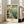 May include: Vintage-style travel poster showing Navy Pier in Chicago with ferris wheel, lighthouse, sailboats on blue water, and lakefront buildings in warm teal and cream tones. Displayed in light wood frame leaning against white wall next to beige sectional sofa in bright, naturally-lit living room with large windows.