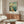 May include: Vintage-style travel poster featuring Chicago's Navy Pier with ferris wheel, pier extending into blue water with sailboats, and "Illinois" text at top, displayed in thin frame above mid-century modern walnut credenza with white upholstered chair and glass coffee table in neutral room setting.