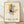 May include: Framed abstract art print in light wood frame leaning against white textured wall on wooden floor. Artwork features geometric composition with yellow, blue, red, and pink rectangular shapes intersected by black linear grid lines on cream background. Modern minimalist room setting with soft natural lighting casting shadows.