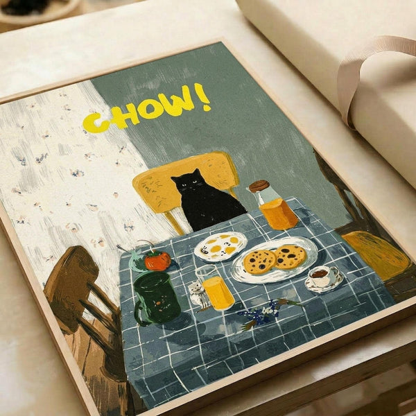 Illustrated poster print featuring a black cat sitting in a yellow armchair at a breakfast table. The scene shows a checkered blue tablecloth with fried eggs, cookies, orange juice, and coffee. Large yellow "CHOW!" text appears at the top against sage green and cream walls. The artwork has a cozy, hand-painted style with warm colors and domestic breakfast setting details.