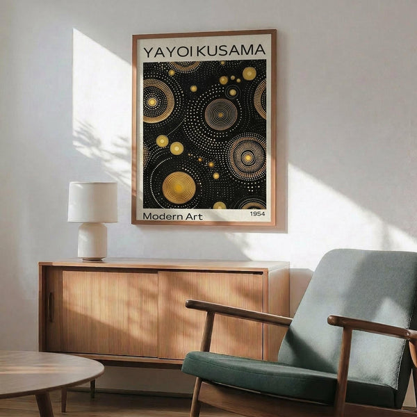 May include: Framed art print featuring black background with golden yellow dotted circular patterns in varying sizes, hung above wooden sideboard with table lamp. Mid-century modern room setting with sage green upholstered chair, round coffee table, and natural sunlight casting shadows on white wall.