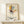 May include: Framed Paul Klee abstract art print displayed on light wooden shelf against cream wall. Artwork features geometric shapes in yellow, red, blue, and black with intersecting lines on beige background. Natural wood frame surrounds the poster. Small wrapped gift box with greenery sits beside the frame, creating minimalist modern home decor scene.