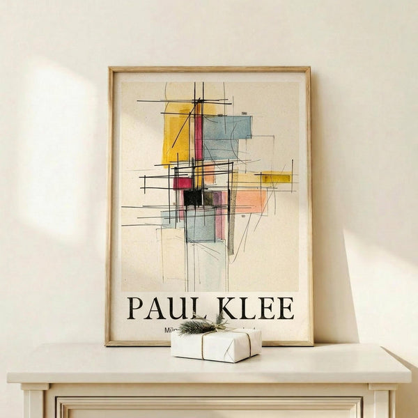 May include: Framed Paul Klee abstract art print displayed on light wooden shelf against cream wall. Artwork features geometric shapes in yellow, red, blue, and black with intersecting lines on beige background. Natural wood frame surrounds the poster. Small wrapped gift box with greenery sits beside the frame, creating minimalist modern home decor scene.