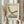 May include: Person holding framed vintage-style poster featuring olive green mid-century modern lounge chair with crossed metal legs. Cream background with "1983 Visions Timeless Design" text in brown. Light wood frame, dried pampas grass visible, neutral beige clothing and curtains in soft natural lighting.