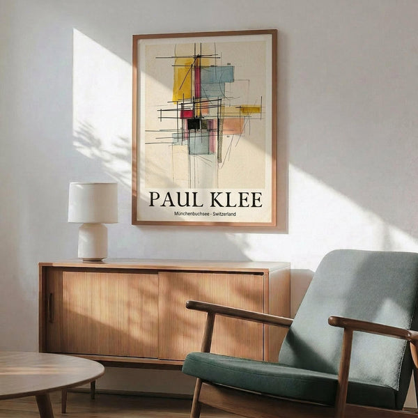 May include: Framed abstract art print featuring geometric shapes in yellow, blue, red, and green with black linear elements on cream background, displayed above mid-century modern wooden credenza with table lamp, next to sage green upholstered armchair with wooden frame in sunlit room with white walls