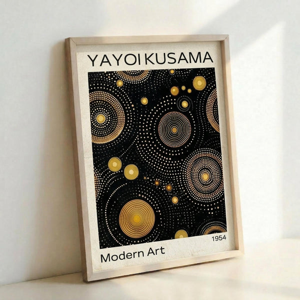 May include: Framed art print leaning against white wall showing abstract pattern of golden yellow circles and dots on black background, displayed in light wood frame on light wooden surface