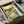 May include: Japanese woodblock print in black frame showing serene landscape with cherry blossoms, green hills, rocky stream, and pale moon in peachy sky. Print sits in open cardboard shipping box with tissue paper and wooden dowels for protection. Traditional ukiyo-e art style with soft earth tones and detailed nature scene.