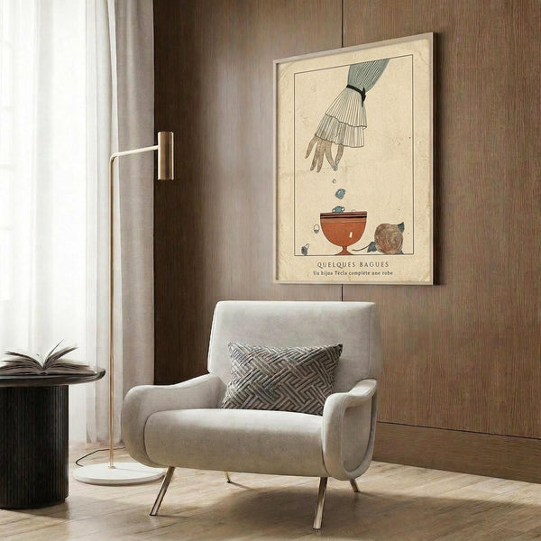 May include: Vintage 1920s Art Deco poster featuring an elegant hand with layered white sleeve cuffs dropping objects into a terracotta bowl, displayed in light wood frame on dark wood paneled wall above cream upholstered armchair with geometric patterned pillow, brass floor lamp and side table nearby