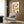 May include: Colorful illustrated poster featuring twelve diverse portrait drawings in a grid layout with "sois unique" text at top, displayed in light wooden frame on wood paneled wall above beige upholstered armchair with geometric patterned pillow, modern floor lamp and side table with open book nearby