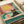 May include: Vintage-style poster print showing a cool black cat wearing yellow sunglasses lounging by a swimming pool with turquoise water. A red drink with citrus slice and striped straw sits nearby on the pool deck. Large yellow sun in coral-pink sky above tiled pool area. Retro illustration style with muted colors displayed as wall art print in neutral room setting.