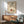 May include: Framed vintage French art print displayed on white wall above wooden sideboard, showing illustrated hand dropping rings into bowl with French text below. Mid-century modern living room setting with teal upholstered chair, round wooden coffee table, and ceramic table lamp. Warm natural lighting creates shadows across the scene.