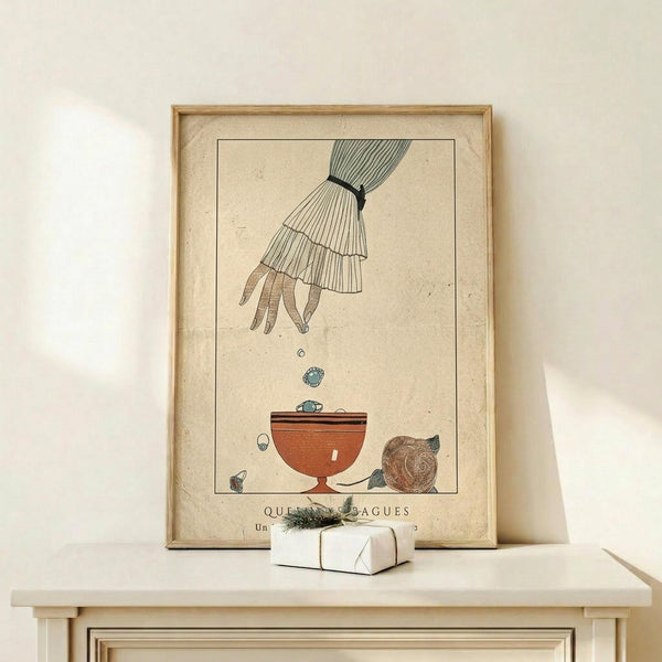 May include: Vintage art print in wooden frame showing an elegant hand dropping jewelry into a terracotta bowl. The illustration features delicate line work on aged cream paper, depicting a feminine hand with ruffled sleeve cuff releasing rings and gems. Displayed on light wood console with small wrapped gift, against neutral wall with soft natural lighting.