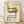 May include: Framed vintage-style poster featuring a modernist cantilever chair with woven cane back, blue upholstered seat, and black tubular steel frame against cream background with yellow circle accent. Text reads "1986 Design Revolution" with small descriptive paragraphs below. Natural wood frame sits on light wooden floor against white textured wall with soft shadows.