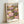 May include: Framed poster print featuring colorful water lilies in pink, purple, yellow and white with green lily pads on dark background, displayed in light wood frame leaning against white wall. Text reads "YAYOI KUSAMA" at top, "Modern Art" and "1984" at bottom. Artwork shows painterly floral pattern in soft, muted tones with dotted textures throughout.