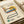 Vintage-style poster featuring a modernist cantilever chair illustration with colorful geometric shapes - yellow circle, blue and red stripes, dotted pattern elements. Black tubular chair frame against cream background with "1986 DESIGN REVOLUTION" text at top. Retro design aesthetic with descriptive text blocks below. Poster shown flat on neutral surface with rolled paper tubes nearby.