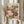 May include: Person holding framed poster featuring colorful water lilies in pink, yellow, and purple tones with green lily pads on dark water background. Light wood frame against cream curtains. Person wears beige ruffled sleeves and holds dried wheat stalks in other hand.