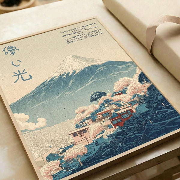 Japanese woodblock print style artwork showing Mount Fuji in the background with traditional buildings and pink cherry blossoms in the foreground. The print features blue and teal mountain slopes, peachy-pink flowering trees, and traditional architecture nestled among the landscape. Japanese characters appear on the left side. The artwork is displayed on cream-colored paper in what appears to be an open book or portfolio format.