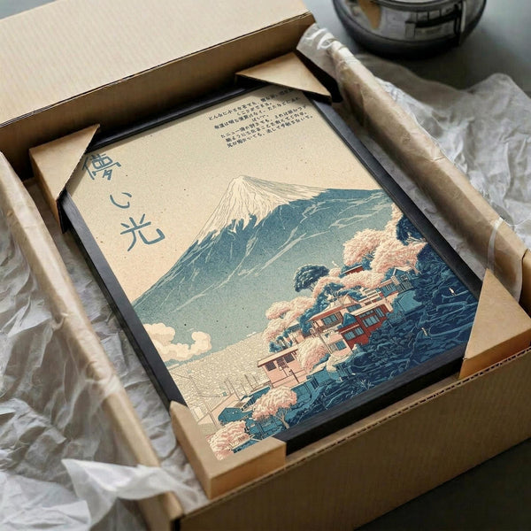 May include: Japanese woodblock-style print showing Mount Fuji with snow-capped peak, traditional buildings nestled among autumn trees with orange foliage, and turbulent blue waves in foreground. Artwork features muted teal, cream and coral tones with vertical Japanese text on left side. Print is displayed in black frame inside cardboard shipping box with protective tissue paper and wooden dowels for packaging.