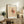 May include: Framed Paul Klee modernist art print displayed on rustic wooden sideboard in warm-toned living room. Abstract artwork features geometric shapes with coral and peach watercolor washes on cream background. Scene includes fern plant, ceramic vase, stacked books, and brown leather furniture in soft natural lighting.