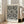 May include: Large framed art print leaning against white wall next to beige sofa in bright living room. Black and white dotted pattern artwork resembles organic cellular or spotted texture with "YAYOI KUSAMA JAPAN 1945" text at bottom. Natural wood frame, approximately 3 feet tall, positioned on light hardwood floor near windows with natural daylight streaming in.