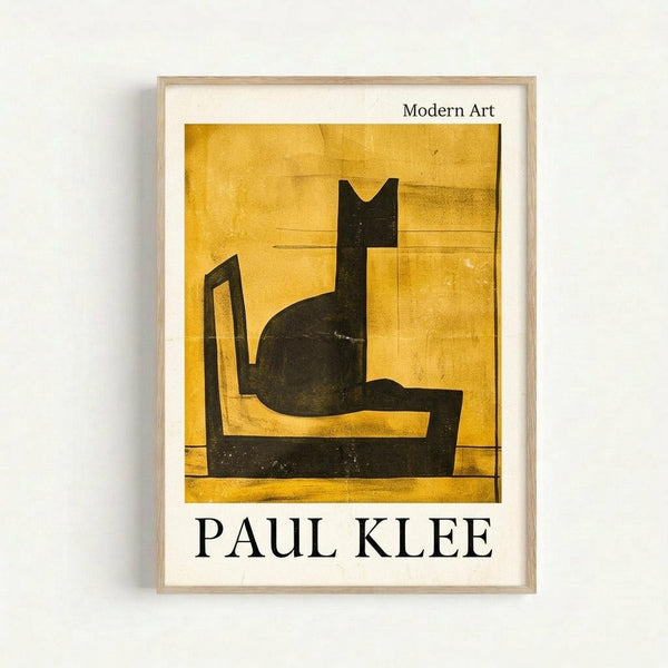 May include: Framed art print hanging on white wall showing Paul Klee's abstract artwork featuring a stylized black cat silhouette against golden yellow background. The minimalist poster has "Modern Art" at top and "PAUL KLEE" at bottom in black text, displayed in light wood frame with white matting.