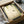 May include: Framed botanical print featuring green hummingbird flying among hanging ferns and trailing vines on cream background, displayed in black frame inside cardboard shipping box with protective tissue paper wrapping