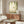 May include: Botanical wall art featuring a hummingbird among hanging ferns and trailing vines on a cream background, displayed above a walnut wood credenza in a minimalist living room with white upholstered chair, glass coffee table, and modern lighting fixtures