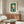 May include: Framed Kandinsky abstract art print featuring geometric shapes in teal, orange, and cream colors hanging above a wooden mid-century sideboard. Modern living room setting with white curved chair, glass coffee table, and minimalist decor. The artwork shows circular and angular forms in Kandinsky's distinctive Bauhaus style against a dark green background.