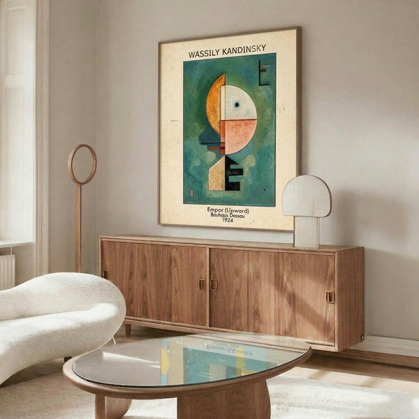 May include: Framed Kandinsky abstract art print featuring geometric shapes in teal, orange, and cream colors hanging above a wooden mid-century sideboard. Modern living room setting with white curved chair, glass coffee table, and minimalist decor. The artwork shows circular and angular forms in Kandinsky's distinctive Bauhaus style against a dark green background.