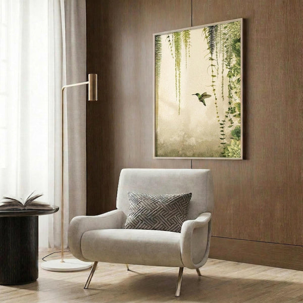 May include: Botanical wall art featuring green hanging ferns and a small hummingbird against a soft cream background, displayed in a gold frame on wood paneled wall above beige upholstered armchair with geometric patterned pillow, alongside brass floor lamp and dark side table with open book