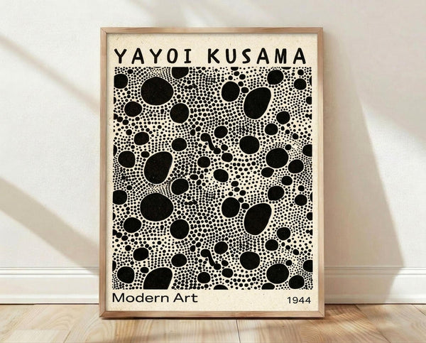 May include: Framed poster with black polka dot pattern in various sizes on cream background, displayed against white wall on light wood floor. Natural wood frame contains densely packed circular dots creating Kusama-inspired infinity net design. Soft natural lighting casts diagonal shadows across the minimalist room setting.