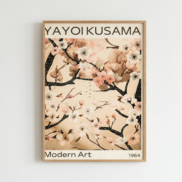 May include: Framed art print hanging on white wall showing cherry blossom branches with pink and white flowers against cream background. Black dotted branches curve across the image with scattered petals. Wooden frame surrounds the poster which displays "YAYOI KUSAMA" at top and "Modern Art 1964" at bottom in black text. Soft, muted color palette with delicate floral illustration in Japanese-inspired style.