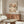 May include: Framed art poster featuring delicate cherry blossom branches with pink and white flowers against cream background, displayed above walnut wood sideboard in modern living room. White curved chair and glass coffee table visible in foreground, natural light creating shadows on warm neutral walls.
