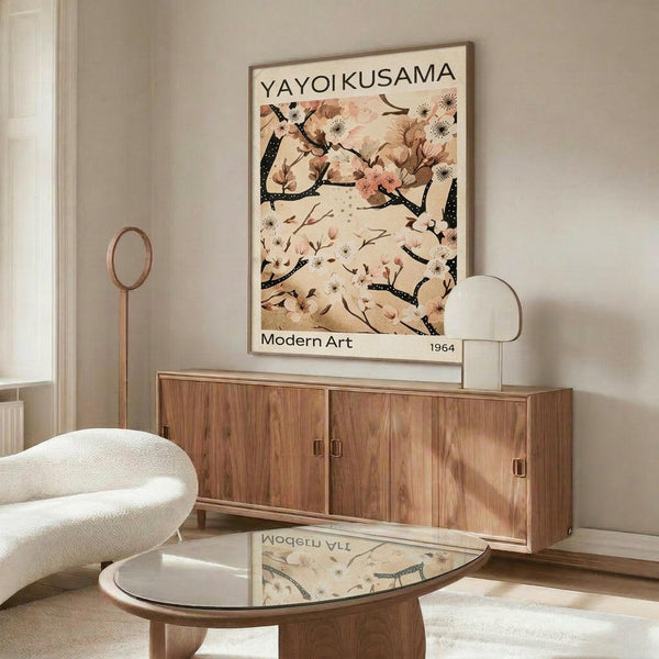 May include: Framed art poster featuring delicate cherry blossom branches with pink and white flowers against cream background, displayed above walnut wood sideboard in modern living room. White curved chair and glass coffee table visible in foreground, natural light creating shadows on warm neutral walls.