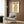 May include: Vintage-style poster featuring stylized orange owl with geometric patterns and Japanese text, displayed in light wooden frame on wood panel wall above beige upholstered armchair with geometric throw pillow, brass floor lamp and round black side table with open book nearby