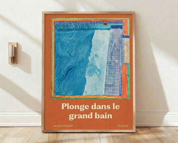 May include: Framed poster with orange background and abstract swimming pool artwork in blues and whites, featuring French text "Plonge dans le grand bain". The print shows wavy water patterns, geometric tiles, and splashing effects. Natural wood frame leaning against white wall on wooden floor, with modern wall sconce visible to the left. Soft natural lighting creates subtle shadows on the wall.