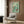 May include: Vintage-style swimming poster with turquoise water background showing three swimmers diving and floating, red "Deep Dive" text at bottom. Framed print hangs on wood-paneled wall above beige upholstered armchair with geometric pillow. Modern floor lamp and side table with open book complete the contemporary living room setting with warm lighting.