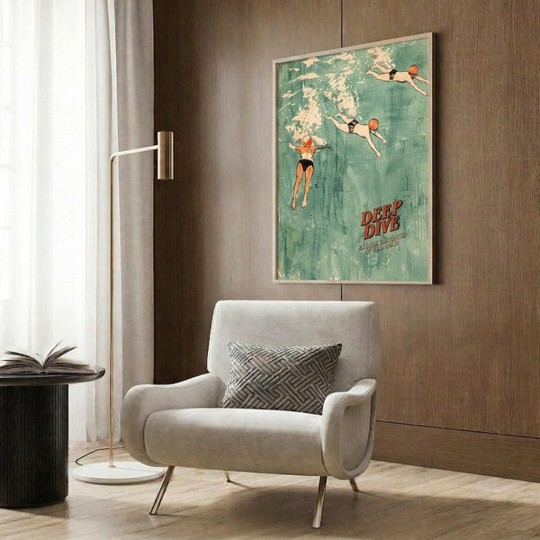 May include: Vintage-style swimming poster with turquoise water background showing three swimmers diving and floating, red "Deep Dive" text at bottom. Framed print hangs on wood-paneled wall above beige upholstered armchair with geometric pillow. Modern floor lamp and side table with open book complete the contemporary living room setting with warm lighting.